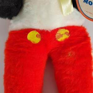 May include: Red plush Mickey Mouse pants with yellow buttons. The pants are made of a soft, fuzzy material. The pants are part of a vintage Mickey Mouse plush toy.