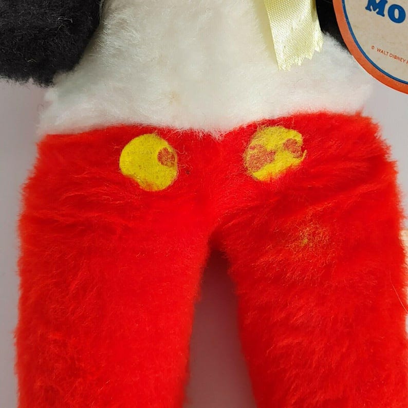 May include: Red plush Mickey Mouse pants with yellow buttons. The pants are made of a soft, fuzzy material. The pants are part of a vintage Mickey Mouse plush toy.