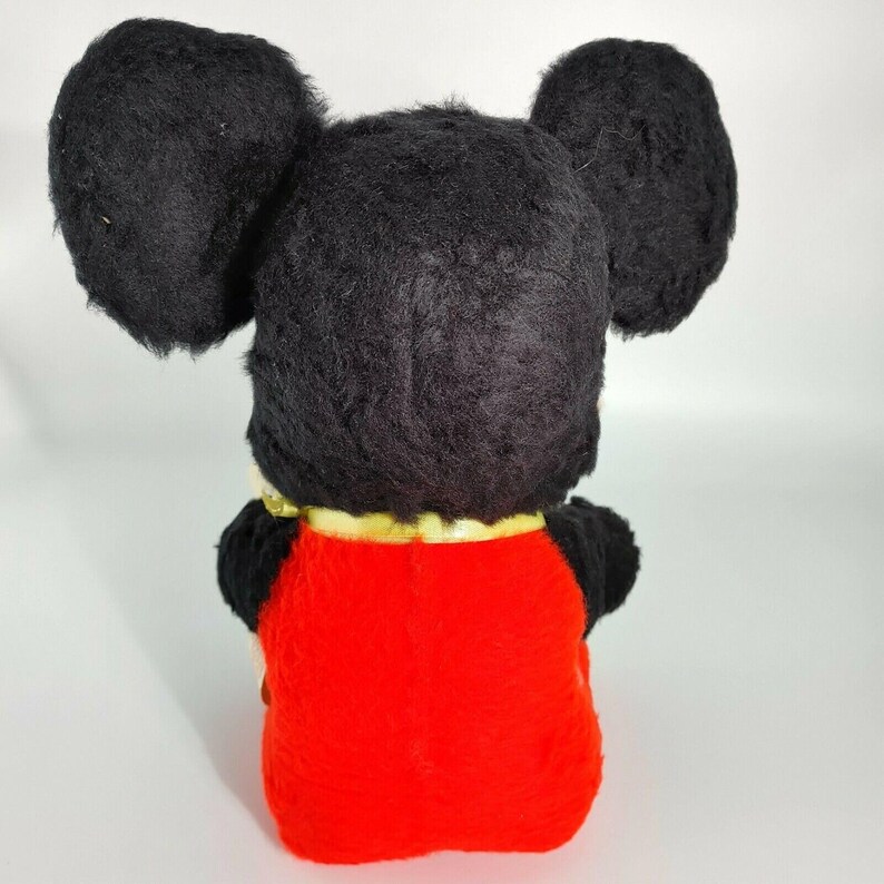 May include: A black and red plush Mickey Mouse toy with large ears. The toy is sitting with its back to the camera. The toy has a gold ribbon around its neck.