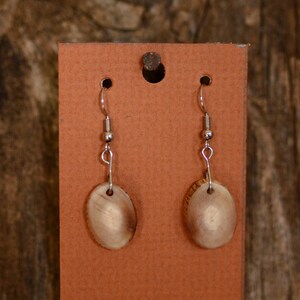 May include: A pair of earrings with oval-shaped wooden pendants. The pendants are a light brown color with a natural wood grain pattern. The earrings are hanging from silver hooks.