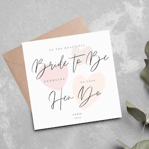 K&ouml;nnte beinhalten: Eine wei&szlig;e Karte mit rosa Herzen und dem Text "To the beautiful Bride to Be Georgina on your Hen Do Paris 2023".