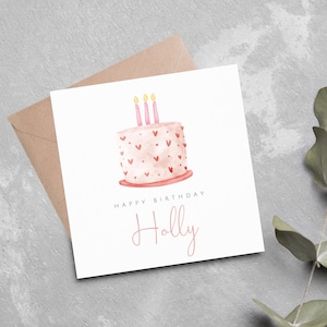 Könnte beinhalten: Eine weiße Karte mit einem rosa und weißen Kuchen mit drei gelben Kerzen und dem Text "Happy Birthday Holly" in rosa.