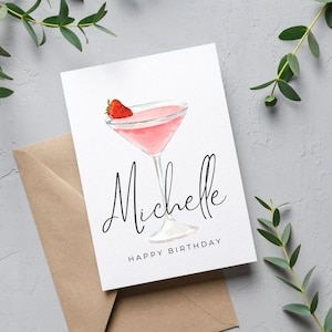 May include: A white card with a pink cocktail with a strawberry garnish. The text "Michelle Happy Birthday" is printed on the card.