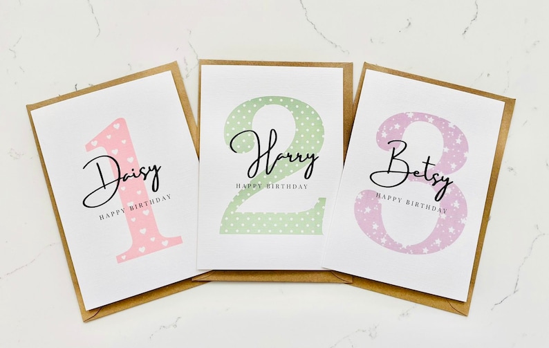 Op de afbeelding: Drie gepersonaliseerde verjaardagskaarten met een nummer, een naam en de tekst "Happy Birthday". De kaarten hebben een roze, groene en paarse achtergrond met een stippen- of sterrenpatroon.