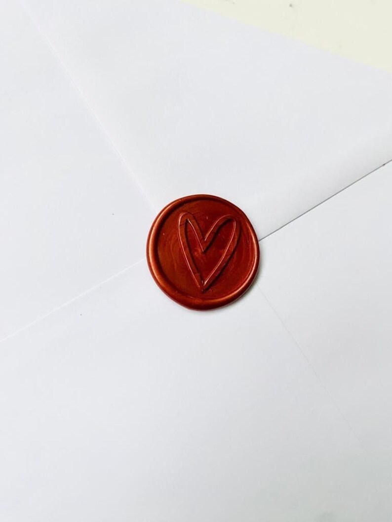 May include: A close-up of a red wax seal with a heart design. The seal is on a white envelope.