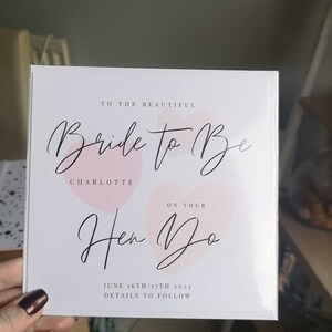 K&ouml;nnte beinhalten: Eine wei&szlig;e Karte mit rosa Aquarellherzen und schwarzer Kalligraphie, auf der steht: "To the beautiful Bride to Be Charlotte On Your Hen Do June 16th/17th 2023 Details to Follow"
