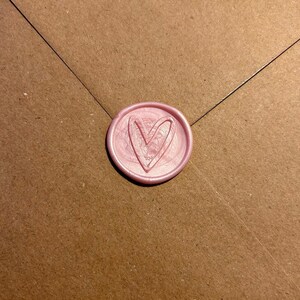 Puede incluir: Un sello de cera rosa con un dise&ntilde;o de coraz&oacute;n.
