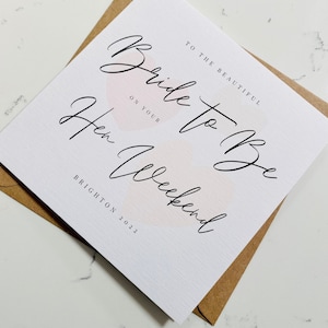 K&ouml;nnte beinhalten: Eine wei&szlig;e Karte mit rosa Aquarell-Akzenten und schwarzer Kalligraphie, auf der steht "An die wundersch&ouml;ne Braut zu sein auf deinem Junggesellinnenabschied Brighton 2022".