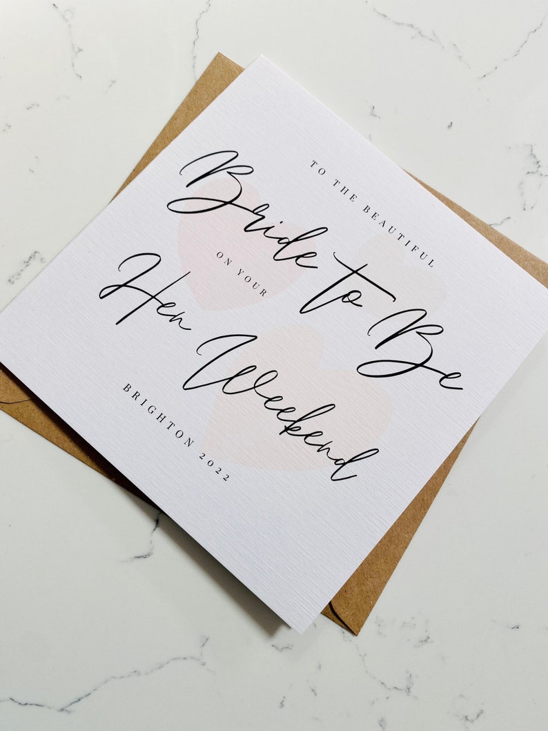 K&ouml;nnte beinhalten: Eine wei&szlig;e Karte mit rosa Aquarell-Akzenten und schwarzer Kalligraphie, auf der steht "An die wundersch&ouml;ne Braut zu sein auf deinem Junggesellinnenabschied Brighton 2022".
