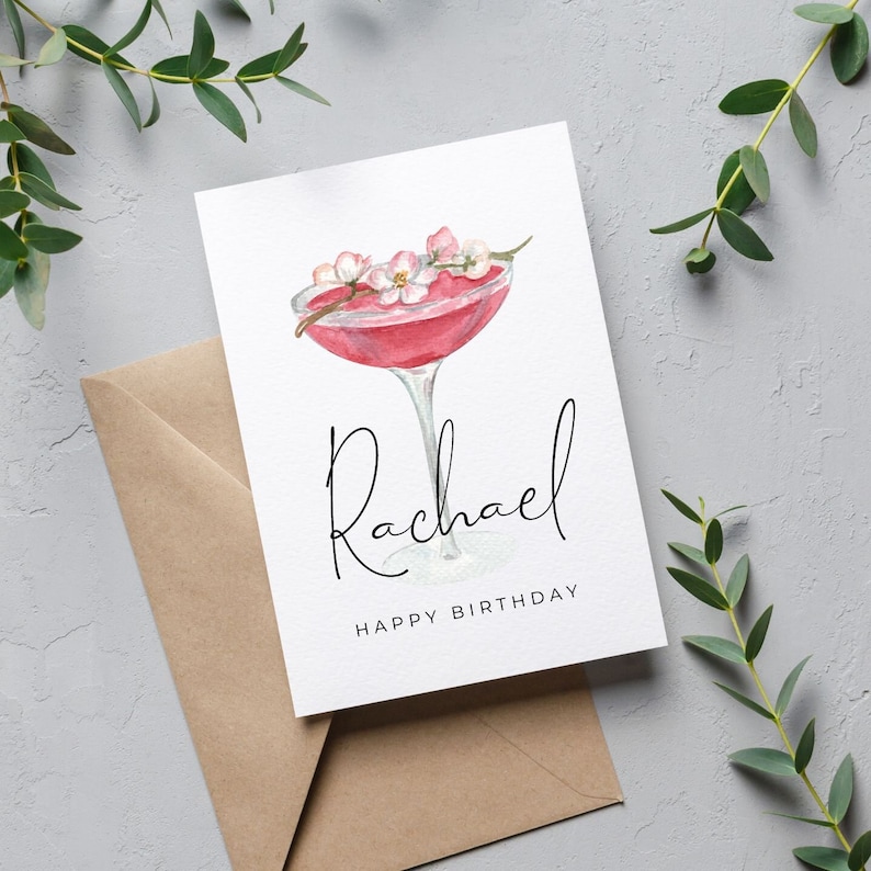 May include: A white card with a pink cocktail with pink flowers on top. The card says "Rachael Happy Birthday".