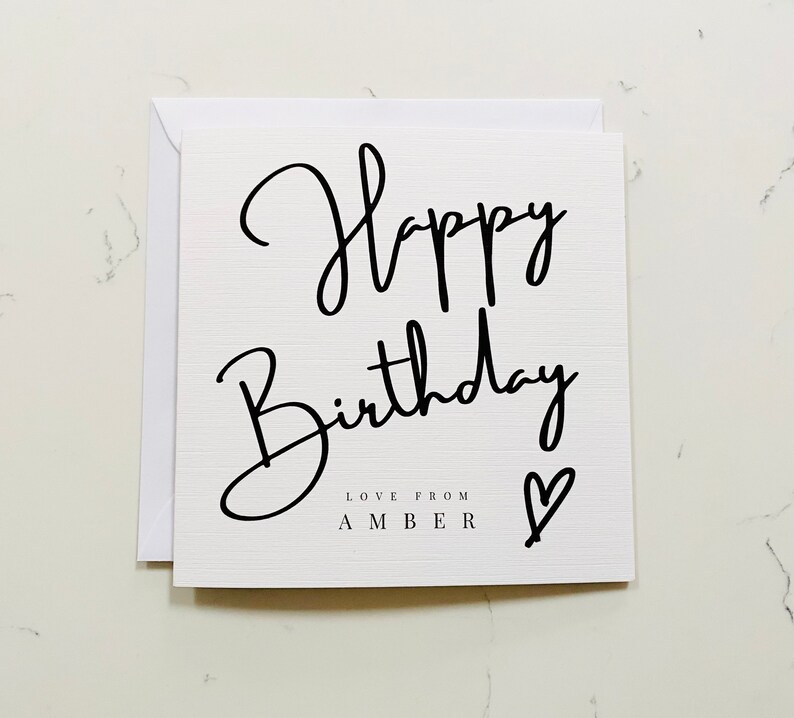 Puede incluir: Tarjeta blanca con escritura negra que dice "Feliz cumplea&ntilde;os" y "Amor de Amber" con un peque&ntilde;o coraz&oacute;n.