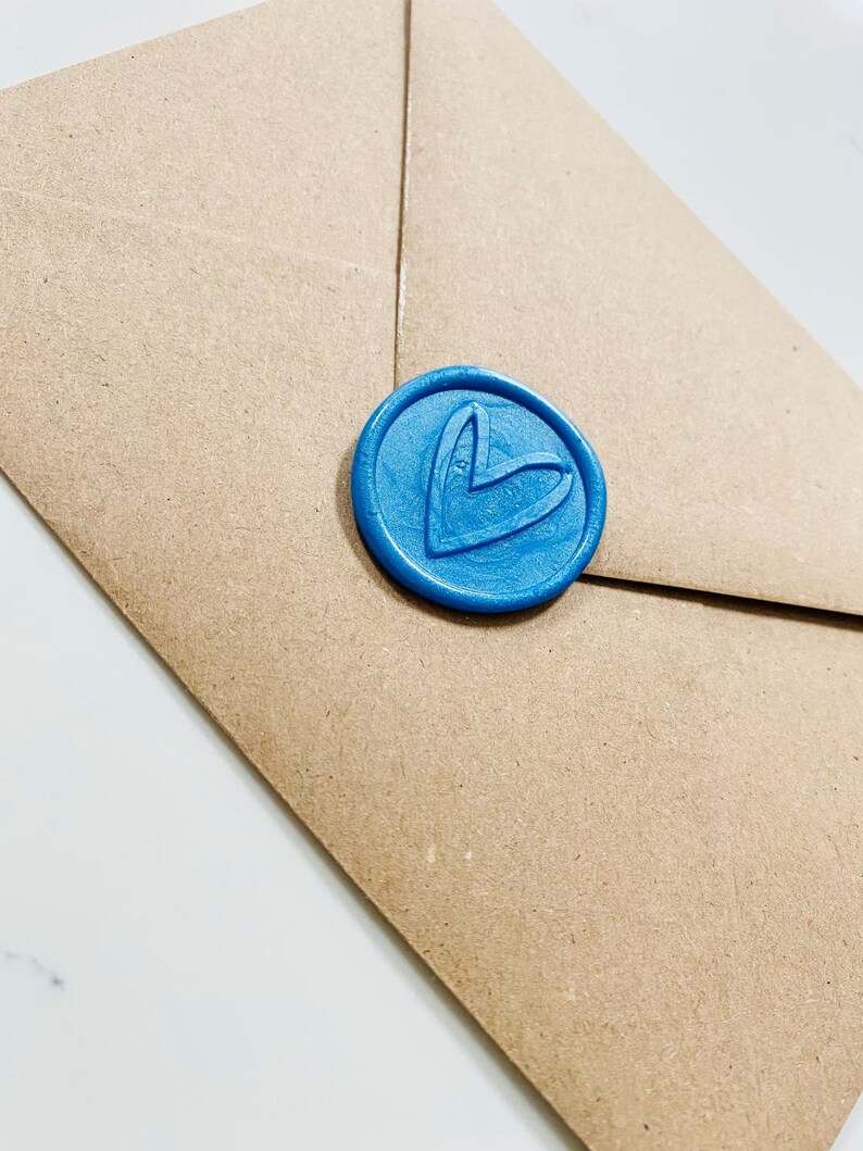 Puede incluir: Un sobre de papel marr&oacute;n con un sello de cera azul. El sello tiene un dise&ntilde;o de coraz&oacute;n.