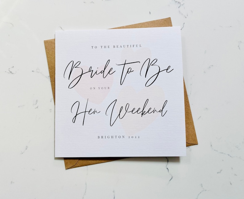 K&ouml;nnte beinhalten: Eine wei&szlig;e Karte mit dem Text "To the beautiful Bride to Be on your Hen Weekend Brighton 2022" in schwarzer Schrift. Die Karte hat einen rosa-wei&szlig;en Aquarellhintergrund.