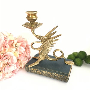 Op de afbeelding: Een gouden messing kandelaar in de vorm van een draak met uitgespreide vleugels. De kandelaar staat op een donkergroen boek met de titel "A Child's Garden of Verses" gedrukt op de rug.