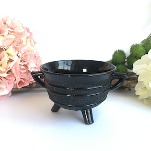 May include: A black glass bowl with three legs and a textured surface. The bowl has a rounded shape and a wide rim.