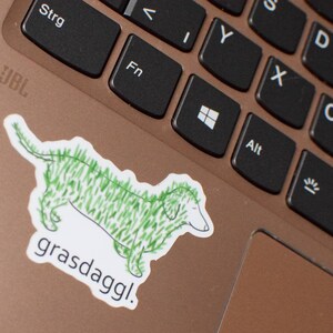 May include: A green and white sticker of a dachshund with the text "grasdaggl!" on a laptop keyboard.