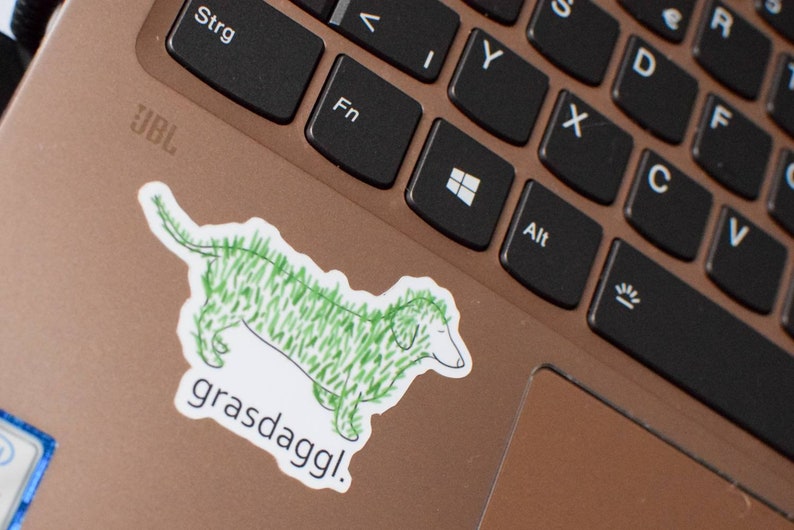 May include: A green and white sticker of a dachshund with the text "grasdaggl!" on a laptop keyboard.