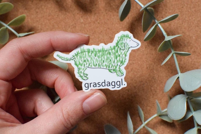 May include: A white sticker with a green cartoon dachshund with the text "grasdaggl." printed below the dog.