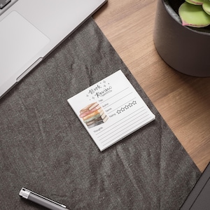 May include: A white notecard with a watercolor illustration of a stack of books. The notecard has the text "Book Review" at the top and includes spaces to write the title, author, genre, rating, and thoughts about the book.