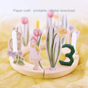 May include: A wooden candle holder featuring paper cutouts of flowers, a girl, and a rabbit. The holder has white candles and a green number three. The text "Paper craft · printable · digital download" is at the top.