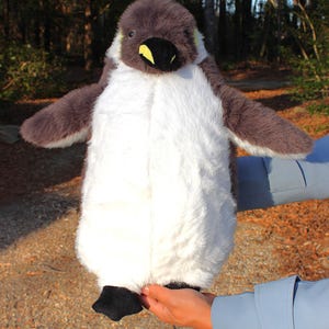 May include: A plush penguin toy featuring soft, fluffy white fur on the chest and belly, contrasted by dark gray fur on the head, back, and wings. The penguin has a black beak with a small yellow accent, dark eyes, and black fabric feet.