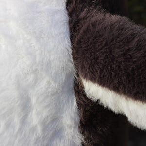 May include: A close-up view of plush fabric featuring a distinct color-blocked design. The material consists of a large section of soft, white faux fur adjacent to a section of dark brown faux fur that features a white trim along the edge.