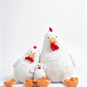 May include: Three plush chicken toys in varying sizes, each featuring soft white fur, bright orange beaks and feet, and a small red comb on top of the head. The figures are arranged in a group, with two larger chickens flanking a smaller chick.