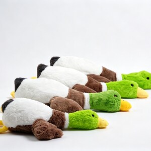 Puede incluir: Una fila de cuatro juguetes de peluche con forma de pato real dispuestos en l&iacute;nea. Cada peluche presenta una cabeza de color verde brillante, un pico amarillo, pecho blanco, alas marrones y una cola negra. Los patos est&aacute;n colocados con pies amarillos.