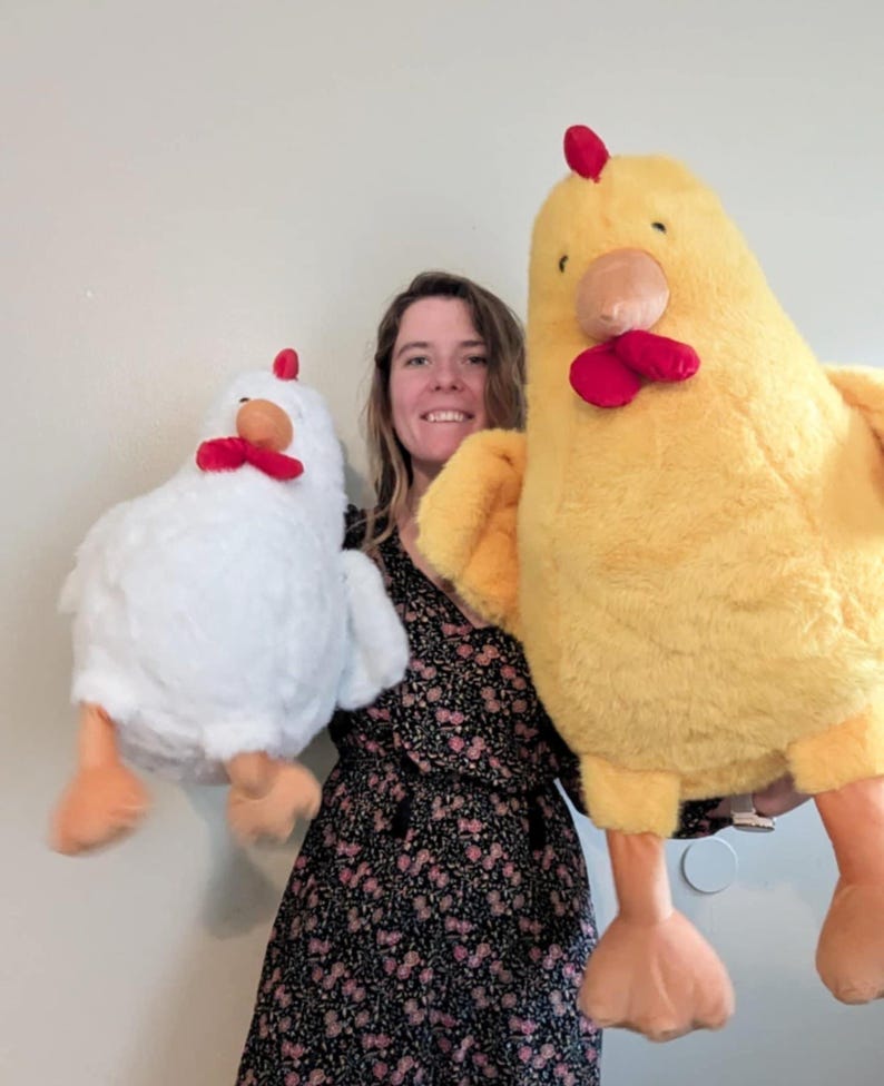 May include: Two plush chicken toys, one large yellow chicken and one smaller white chicken. Both chickens feature soft, fuzzy fabric, bright red combs and wattles, orange beaks, and orange feet. The toys are rounded in shape with wings.