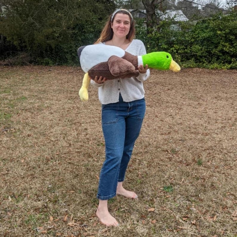 Puede incluir: Un juguete de peluche grande con forma de pato azul&oacute;n que presenta una cabeza verde brillante, un pico amarillo, un anillo blanco en el cuello y un cuerpo marr&oacute;n y blanco. El peluche es suave y texturizado, dise&ntilde;ado para parecerse a un pato salvaje.