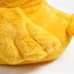 May include: A bright yellow plush toy featuring soft, synthetic fur texture. The object displays a prominent wing-like appendage with three distinct segments and a small, rounded tail section extending from the main body of the stuffed animal.