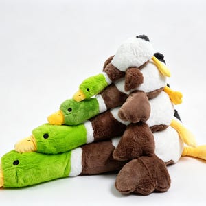 Puede incluir: Una pila de cuatro juguetes de peluche con forma de pato real dispuestos en forma de pir&aacute;mide. Cada pato presenta una cabeza de color verde brillante, un pico amarillo, un anillo blanco en el cuello y un cuerpo marr&oacute;n con textura suave.