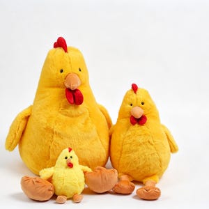 May include: Three plush chicken toys in varying sizes, all featuring bright yellow soft fabric, red combs and wattles, and orange beaks. The set includes one large chicken, one medium chicken, and one small chick, all sitting upright on a plain surface.