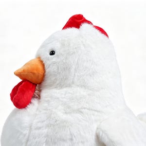 May include: A plush stuffed chicken toy featuring soft white fur, a bright orange beak, a vibrant red comb on top of the head, and a red wattle hanging below the beak. The toy has a small black eye and a rounded body with a visible wing on the side.