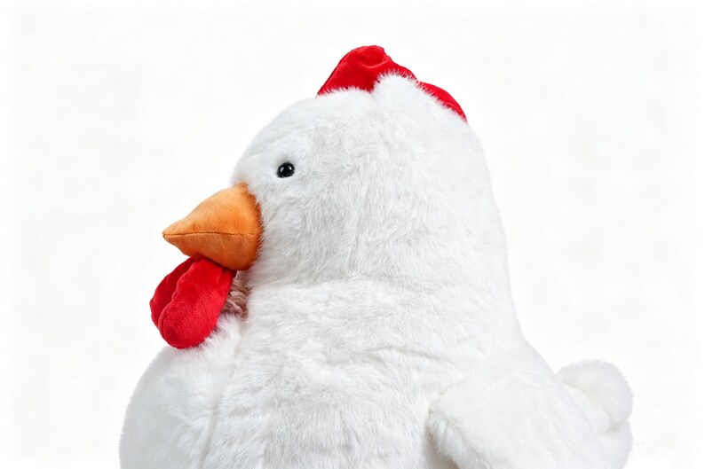 May include: A plush stuffed chicken toy featuring soft white fur, a bright orange beak, a vibrant red comb on top of the head, and a red wattle hanging below the beak. The toy has a small black eye and a rounded body with a visible wing on the side.