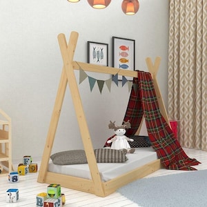 May include: A wooden teepee bed frame with a white mattress, red and black plaid canopy, and a stuffed animal. The bed frame is decorated with a string of colorful flags.