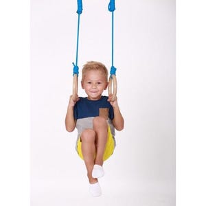 May include: A young person is hanging from blue rope gymnastic rings. The rings are made of wood and have a natural finish. The person is wearing a blue and grey shirt and yellow shorts.