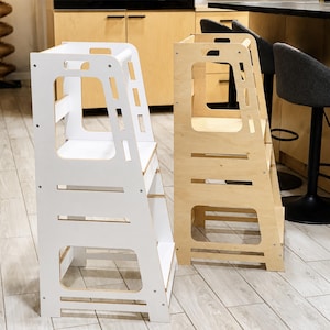 May include: Two standing towers for children, one finished in solid white and the other in natural light wood. Each tower features a tall, open-frame design with a platform, side cutouts, and a safety rail, constructed from flat wooden panels.