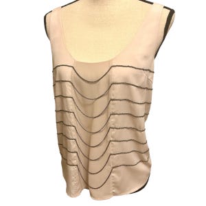 May include: A sleeveless, light pink top with a scoop neckline. The top features multiple horizontal, wavy, dark gray chain-like embellishments across the front. The fabric has a slight sheen, giving it a silky appearance.
