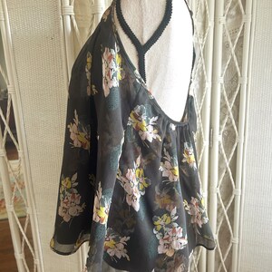 K&ouml;nnte beinhalten: Ein dunkelgraues Neckholder-Top mit einem Blumenmuster in Rosa, Gelb und Gr&uuml;n. Das Top hat einen tiefen R&uuml;ckenausschnitt und zarte Tr&auml;ger. Der Stoff scheint transparent und leicht zu sein.