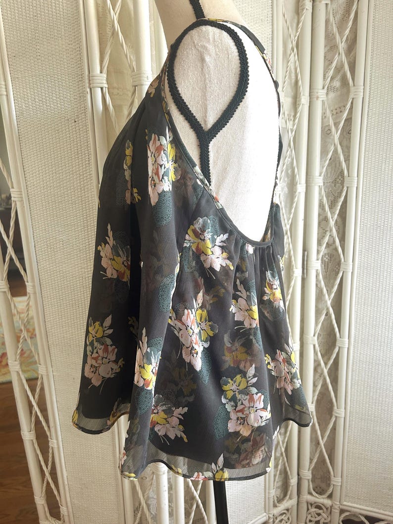 K&ouml;nnte beinhalten: Ein dunkelgraues Neckholder-Top mit einem Blumenmuster in Rosa, Gelb und Gr&uuml;n. Das Top hat einen tiefen R&uuml;ckenausschnitt und zarte Tr&auml;ger. Der Stoff scheint transparent und leicht zu sein.