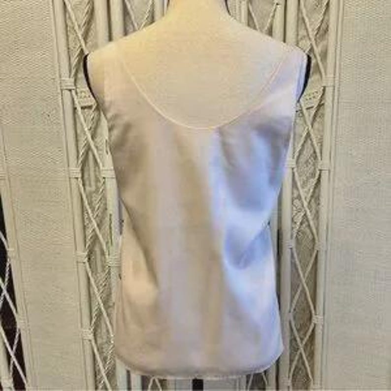 May include: A light pink satin tank top with a scoop neck and a sleeveless design. The tank top is displayed on a mannequin against a neutral background. The fabric has a subtle sheen.