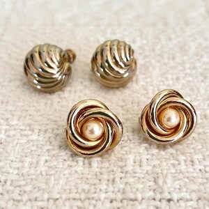 Könnte beinhalten: Vier goldfarbene Ohrringe. Zwei haben ein Spiraldesign mit einem Kunstperlenmittelpunkt, und zwei haben ein geripptes Wirbeldesign. Die Ohrringe befinden sich auf einer weißen, strukturierten Oberfläche. Diese Ohrringe eignen sich für den Alltag oder besondere Anlässe.