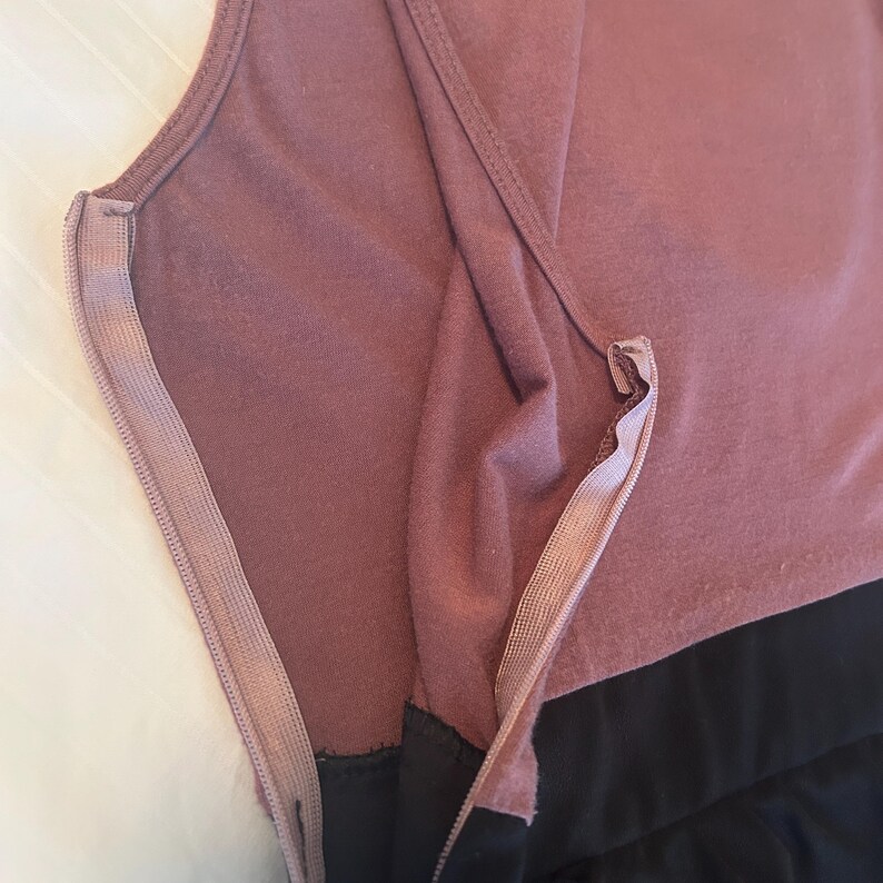 Puede incluir: Primer plano de un vestido sin mangas con un corpi&ntilde;o malva y una falda negra. El vestido presenta una cremallera lateral, que resalta la construcci&oacute;n y la textura de la tela. La tela parece suave y c&oacute;moda.