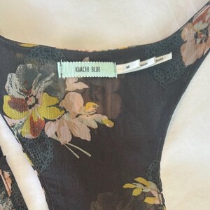 K&ouml;nnte beinhalten: Schwarzes Oberteil mit floralem Print und Rundhalsausschnitt. Das Oberteil hat ein zartes Blumenmuster in Gelb-, Rosa- und Wei&szlig;t&ouml;nen. Das Etikett lautet "KIMCHI BLUE" und "M".