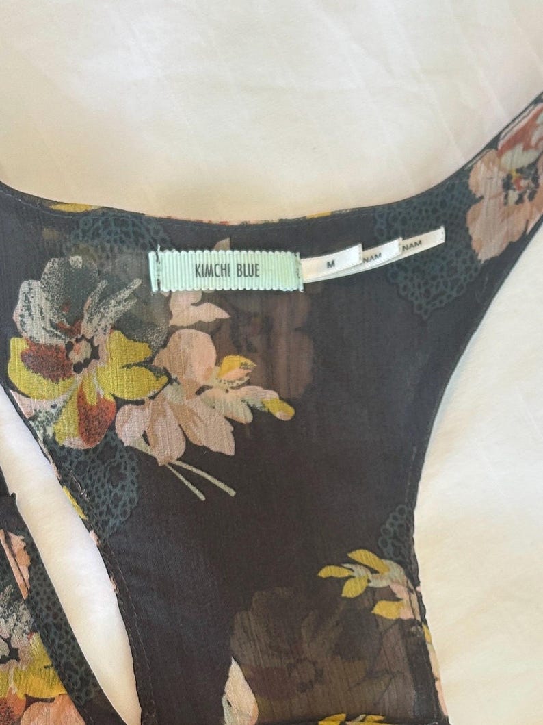 K&ouml;nnte beinhalten: Schwarzes Oberteil mit floralem Print und Rundhalsausschnitt. Das Oberteil hat ein zartes Blumenmuster in Gelb-, Rosa- und Wei&szlig;t&ouml;nen. Das Etikett lautet "KIMCHI BLUE" und "M".