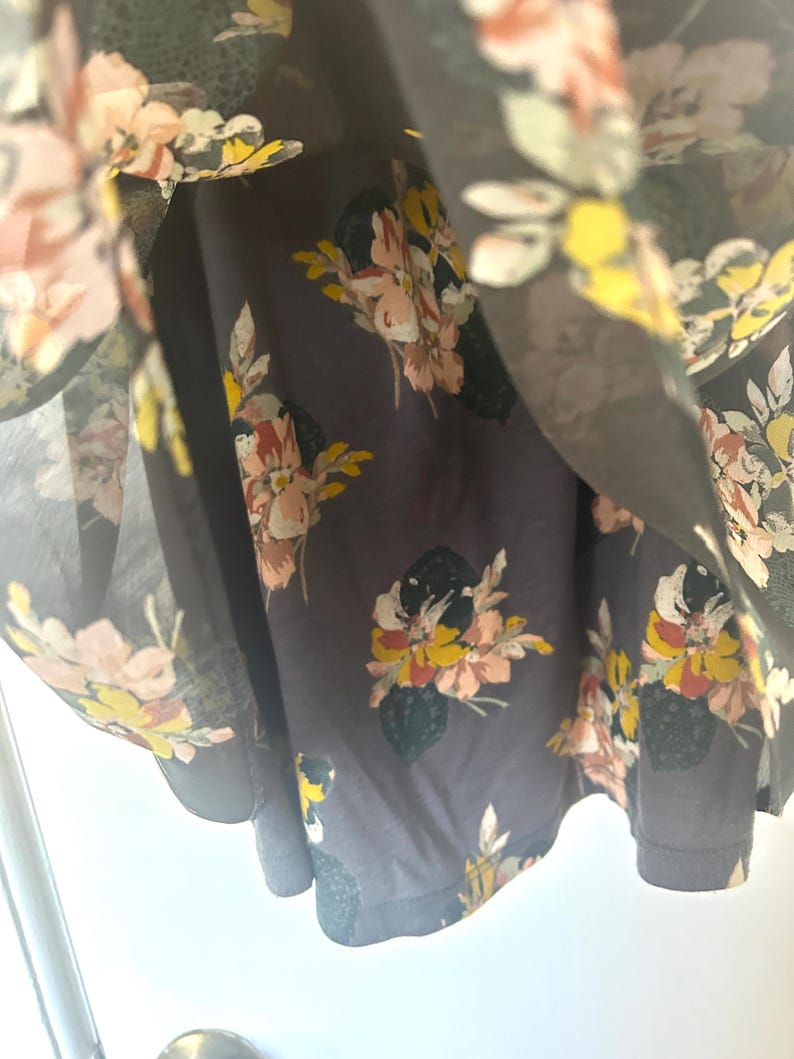 K&ouml;nnte beinhalten: Nahaufnahme eines dunkelgrauen Kleides mit floralem Muster. Die Blumen sind in Rosa, Gelb und Wei&szlig; gehalten, mit gr&uuml;nen Bl&auml;ttern. Der Stoff wirkt leicht und flie&szlig;end.