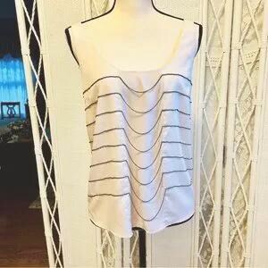 May include: A sleeveless, light pink top with a scoop neck and a decorative, wavy black trim. The trim creates horizontal lines across the front of the top. The top is displayed on a mannequin.