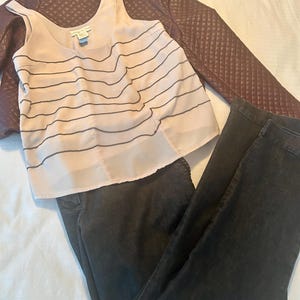 May include: A complete outfit featuring a light pink tank top with black horizontal lines, dark wash jeans, and a burgundy quilted jacket. The tank top has a scoop neck and a tag. The jacket is a dark burgundy color.