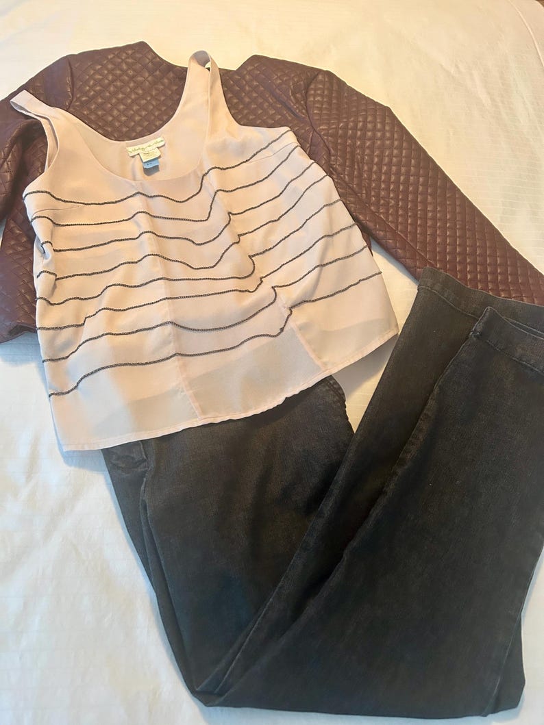 May include: A complete outfit featuring a light pink tank top with black horizontal lines, dark wash jeans, and a burgundy quilted jacket. The tank top has a scoop neck and a tag. The jacket is a dark burgundy color.